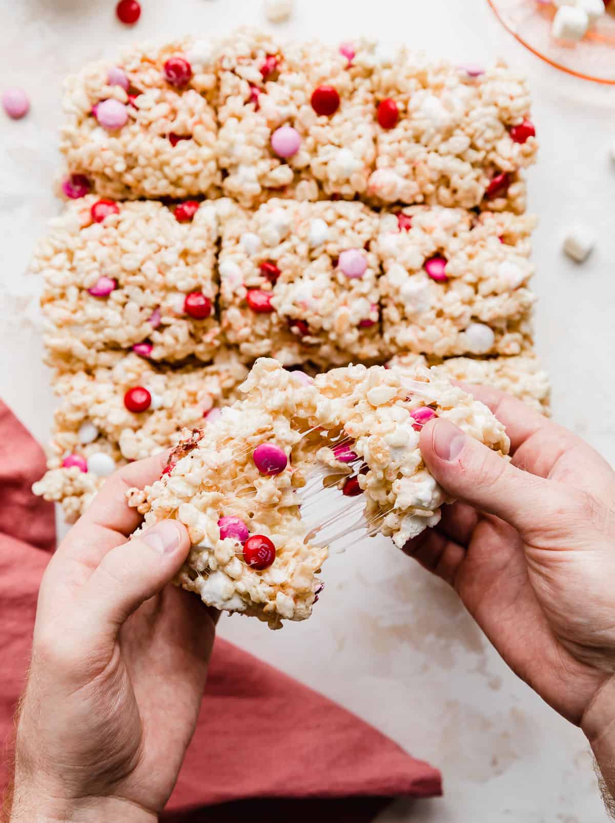 Two hands pulling Valentine Rice Krispie Treats apart showing the melted marshmallows pulling.