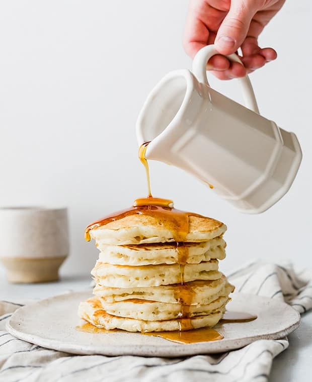 Maple syrup being drizzled over a stack of pancakes.