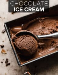 Dark chocolate ice cream in a rectangle bread pan with an ice cream scoop scooping out a ball of the brown ice cream.