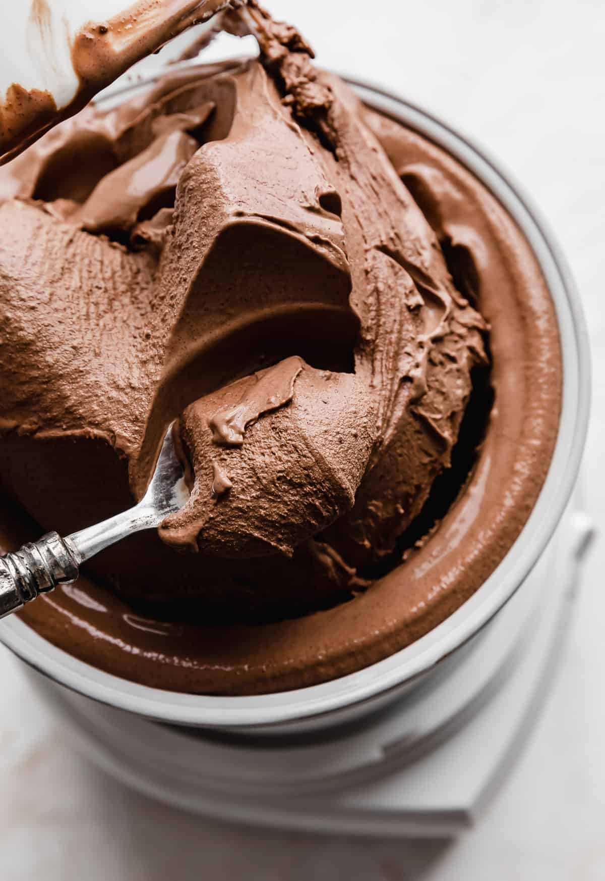 Creamy chocolate ice cream being pulled from an at-home ice cream maker, with a spoon scooping out some of the ice cream.