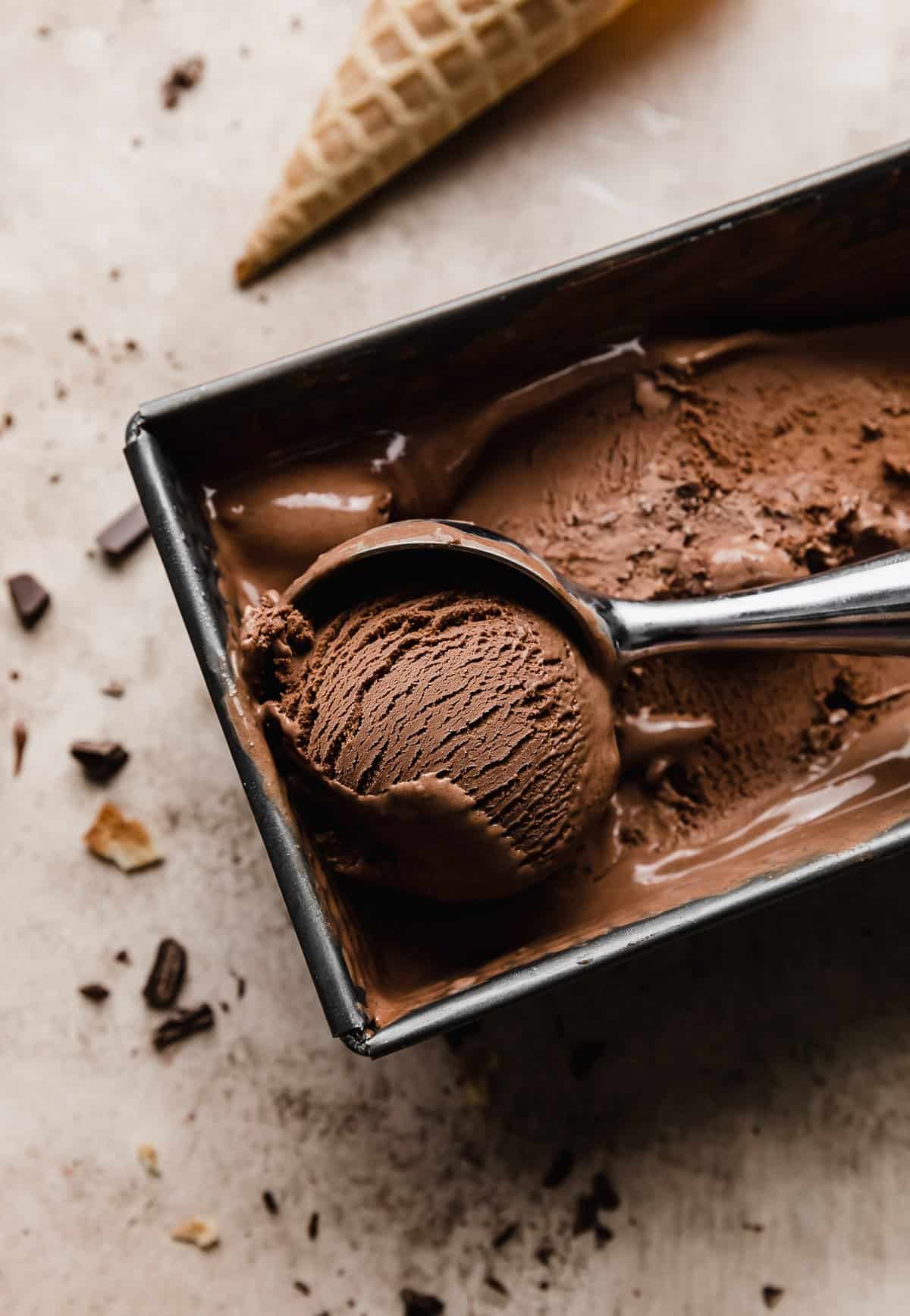 An ice cream scoop rolling out a portion of Homemade Chocolate Ice Cream from a square bread pan.