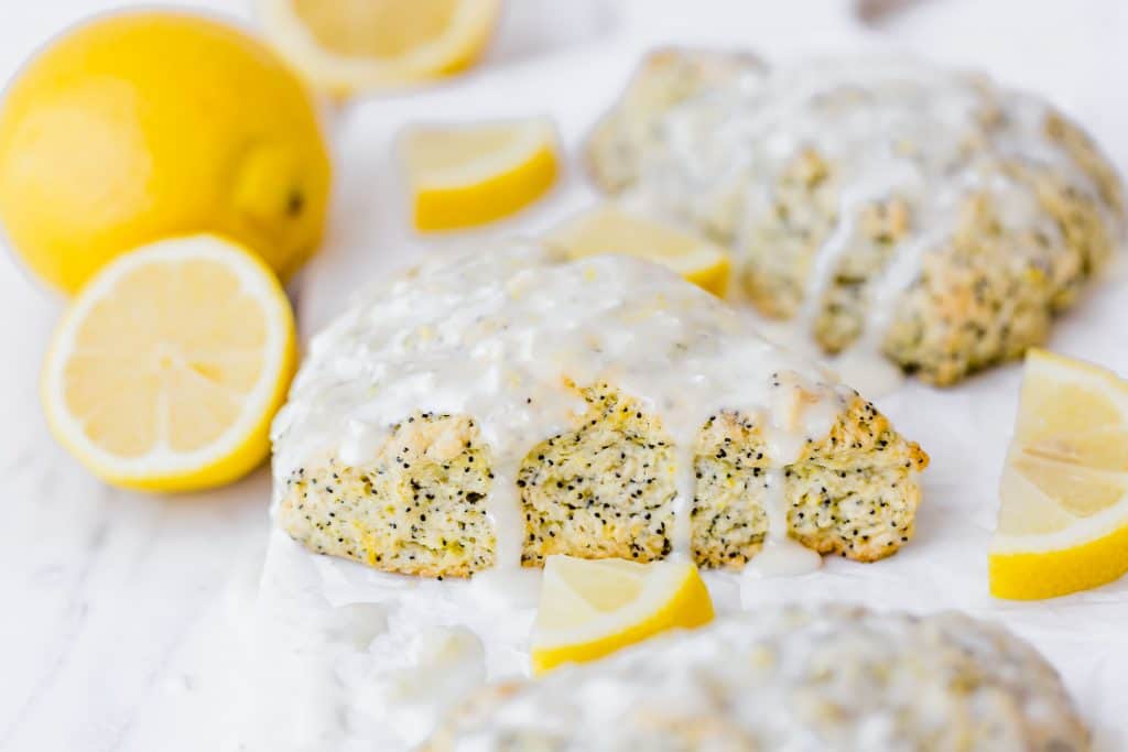 Lemon poppy seed scone with a glaze drizzled overtop, surrounded by fresh lemons.