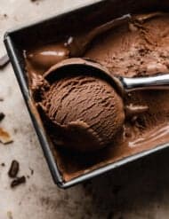 The best chocolate ice cream in a bread pan with an ice cream scooper scooping out a ball of the brown ice cream.