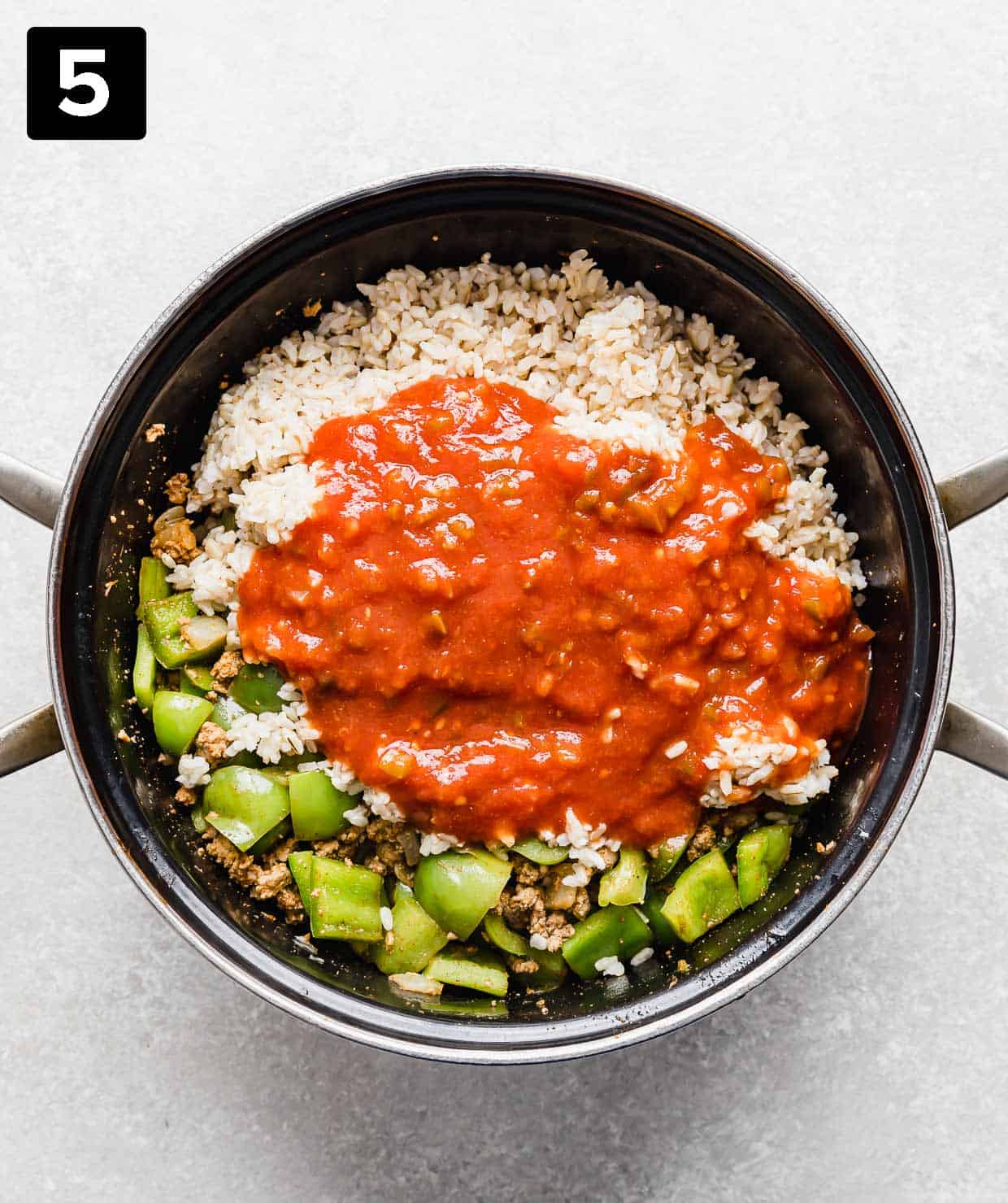 A large pot with rice, chopped green peppers, and salsa in it.