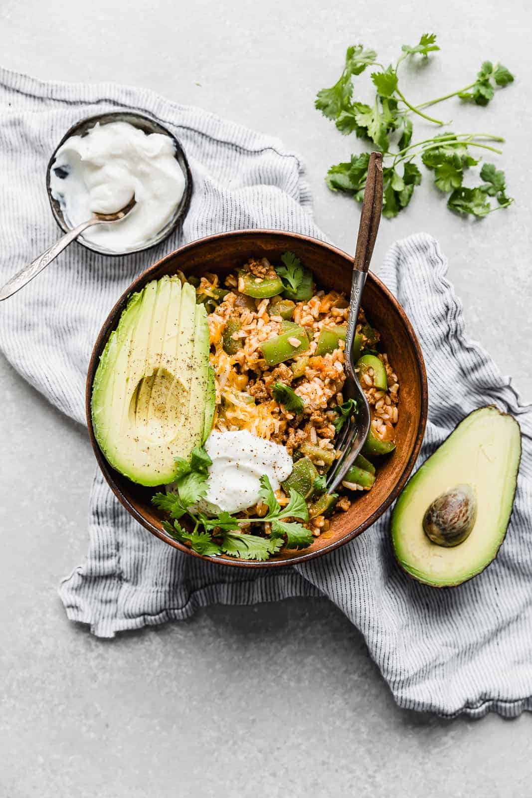 Deconstructed Stuffed Peppers in a brown bowl with a sliced avocado and cilantro for garnish.