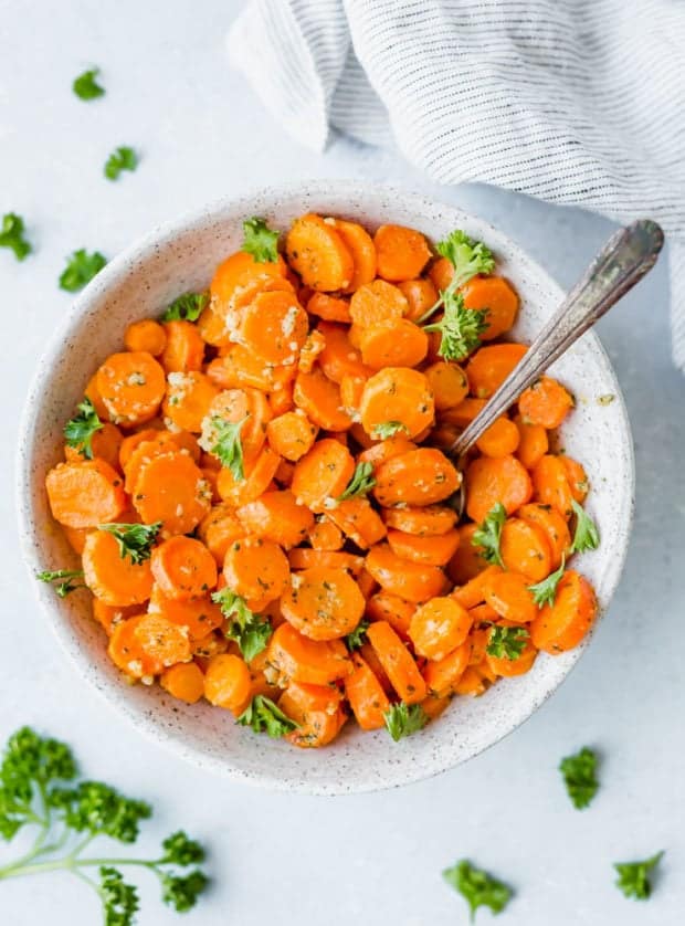 A bowl of roasted carrots garnished with fresh parsley, with a spoon in the bowl.