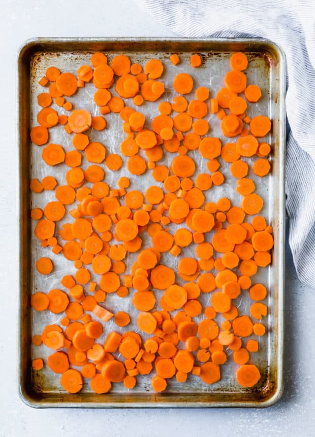 Chopped carrots spread out along a baking sheet, in preparation to make garlic parmesan roasted carrots.