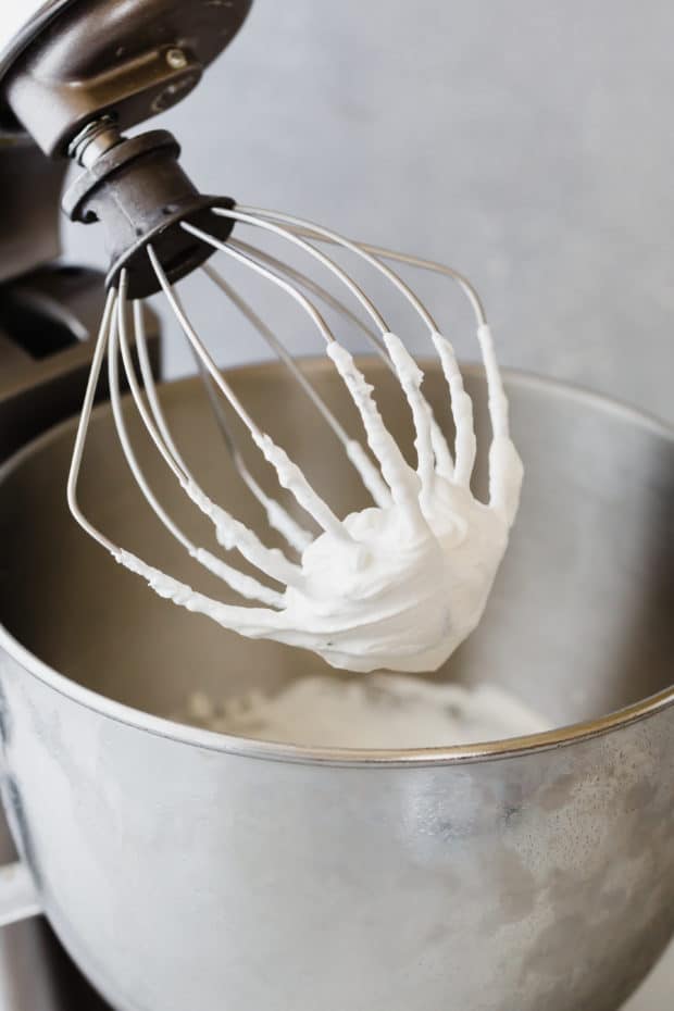 The whisk attachment to a kitchen aid stand covered in greek yogurt whipped cream.