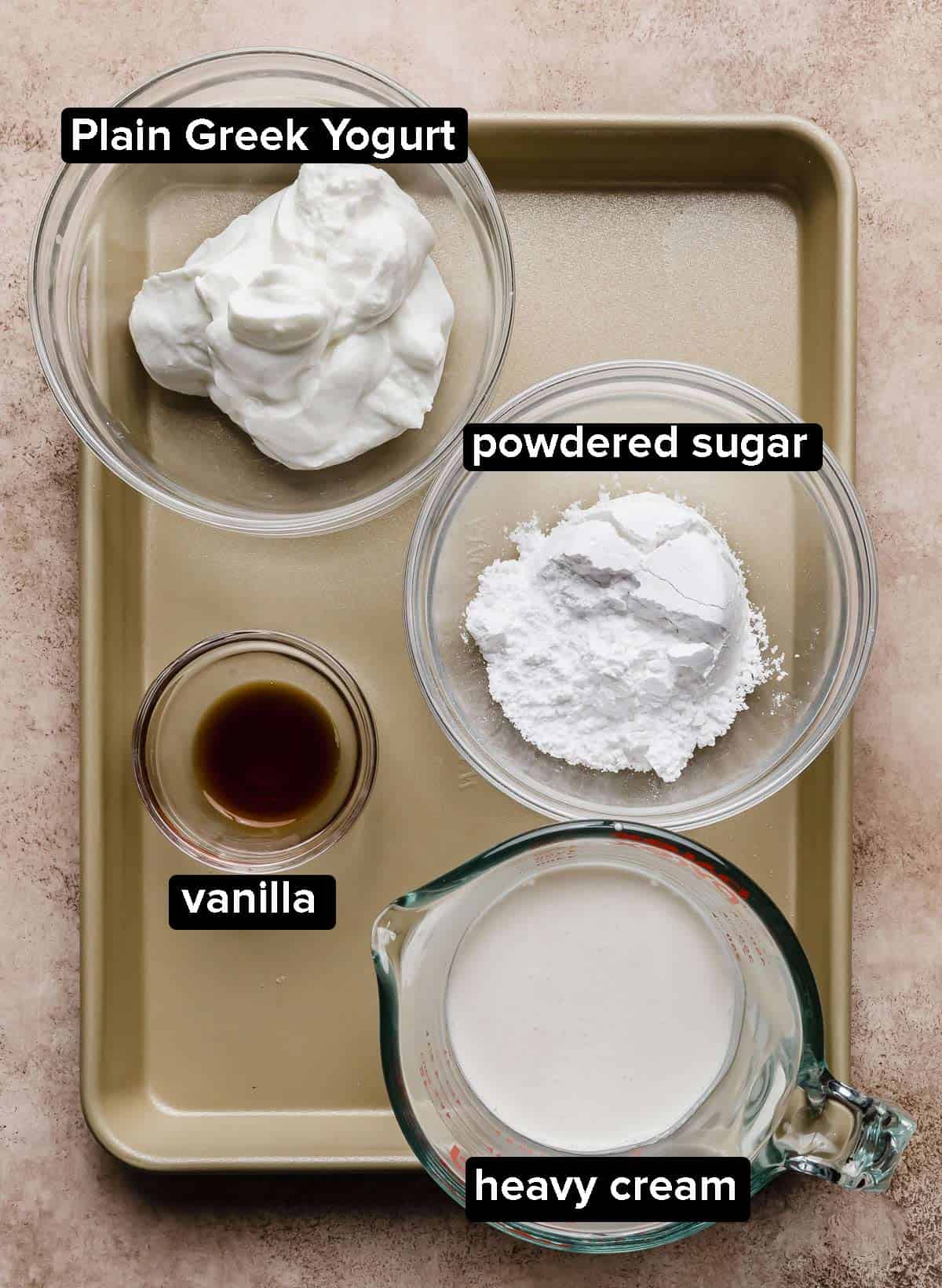 A baking sheet with four glass bowls with ingredients used to make Greek Yogurt Whipped Cream; Greek yogurt, powdered sugar, heavy cream, and vanilla. 