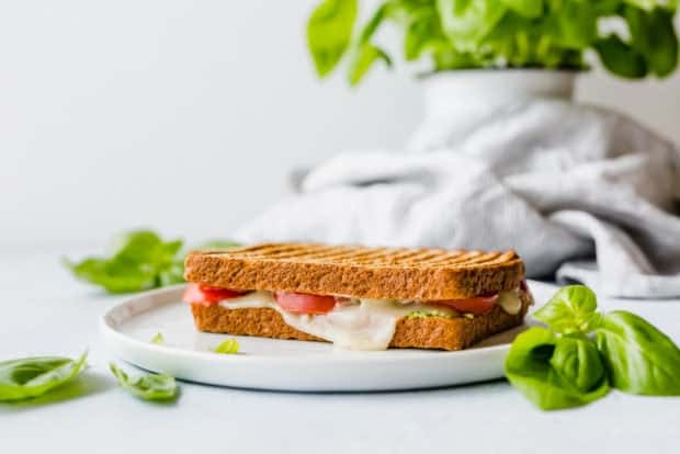 A grilled sandwich with melted mozzarella and fresh tomatoes visible between the slices of bread. 
