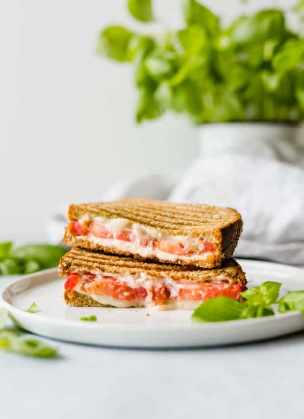 A grilled sandwich cut in half exposing the melty mozzarella, tomatoes, and basil pesto.