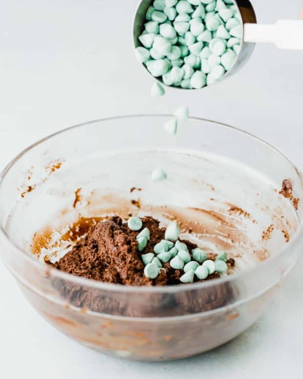 Mint chips being poured into chocolate cookie dough batter.