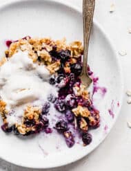 Blueberry crisp on a plate, topped with a scoop of vanilla ice cream.