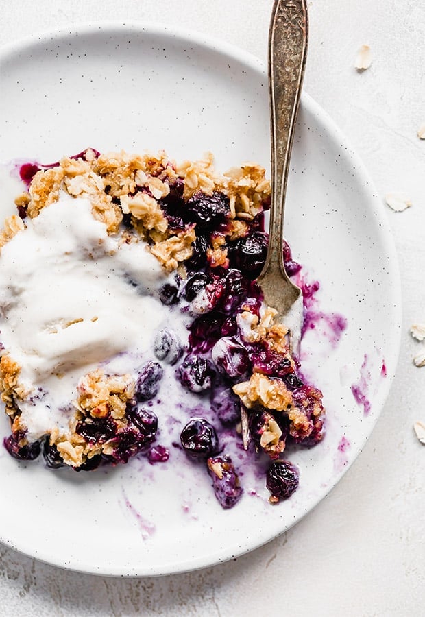 Blueberry crisp on a plate, topped with a scoop of vanilla ice cream.