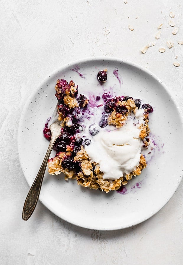 A plate of blueberry crisp topped with vanilla ice cream.