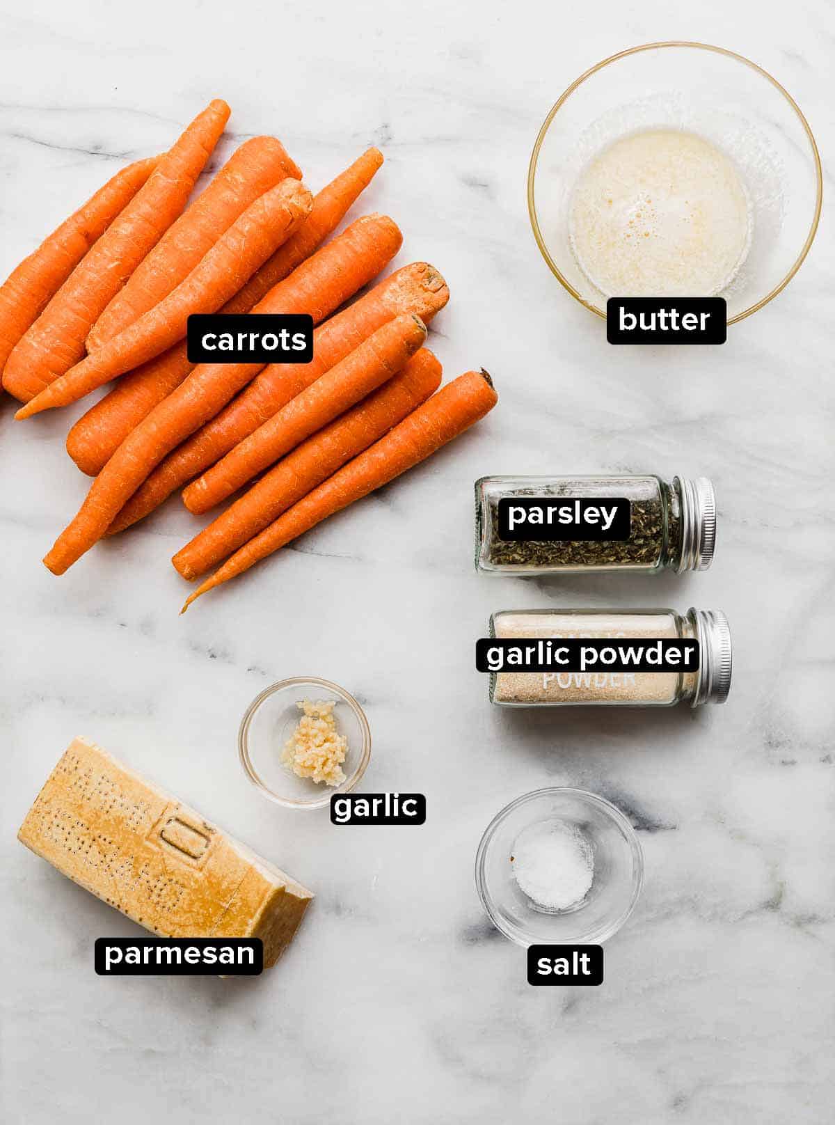 Ingredients used to make Garlic Butter Roasted Carrots on a white background: carrots, butter, garlic, salt, parsley, and parmesan.