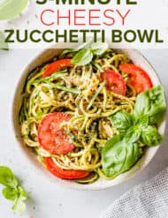 A bowl with zucchini noodles, sliced tomatoes, and fresh basil leaves.
