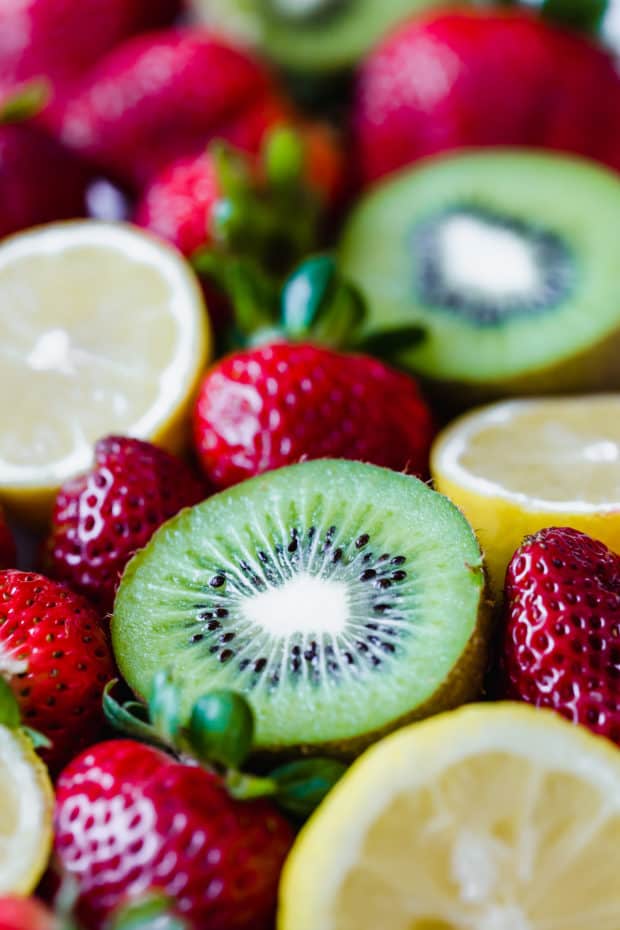 A close up picture of ripe red strawberries and halved lemons and kiwis.