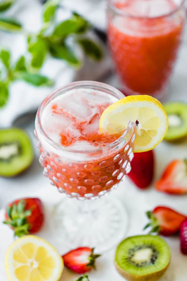 A top view of a tall clear glass full of strawberry kiwi lemonade and a lemon wedge hanging from the edge of the glass.