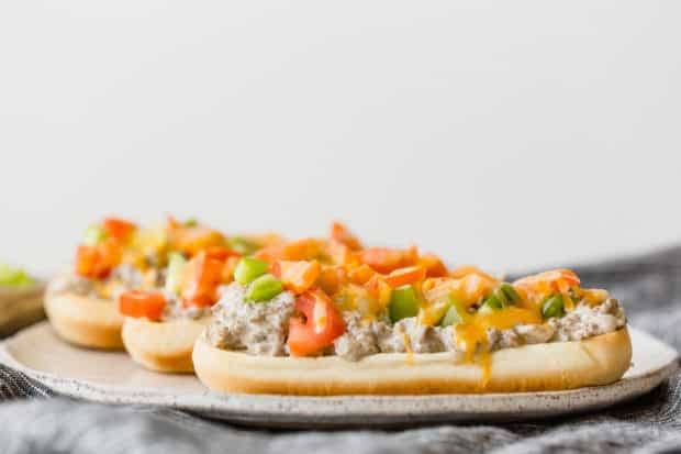 A side view of hoagie buns topped with beef stroganoff, diced tomatoes, green bell peppers, and melted cheese.