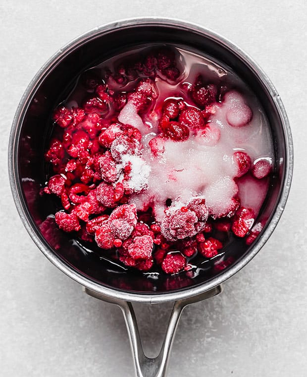 A saucepan full of frozen raspberries, water, and sugar.