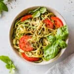 Zucchetti Pasta in a white bowl with nutritional yeast, tomatoes, and fresh basil.