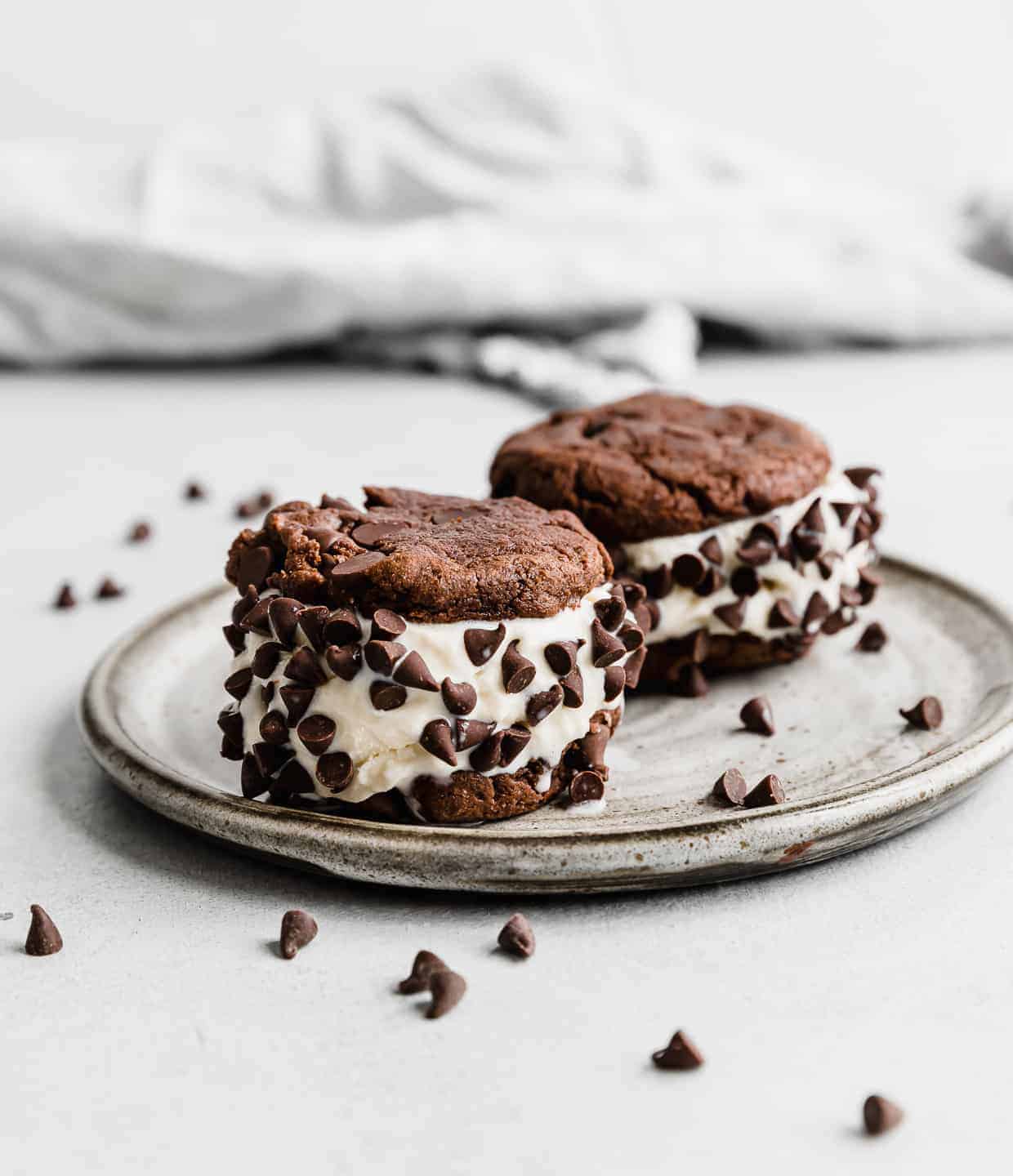 Two Cookie Ice Cream Sandwiches on a gray plate with mini chocolate chips surrounding the plate. 