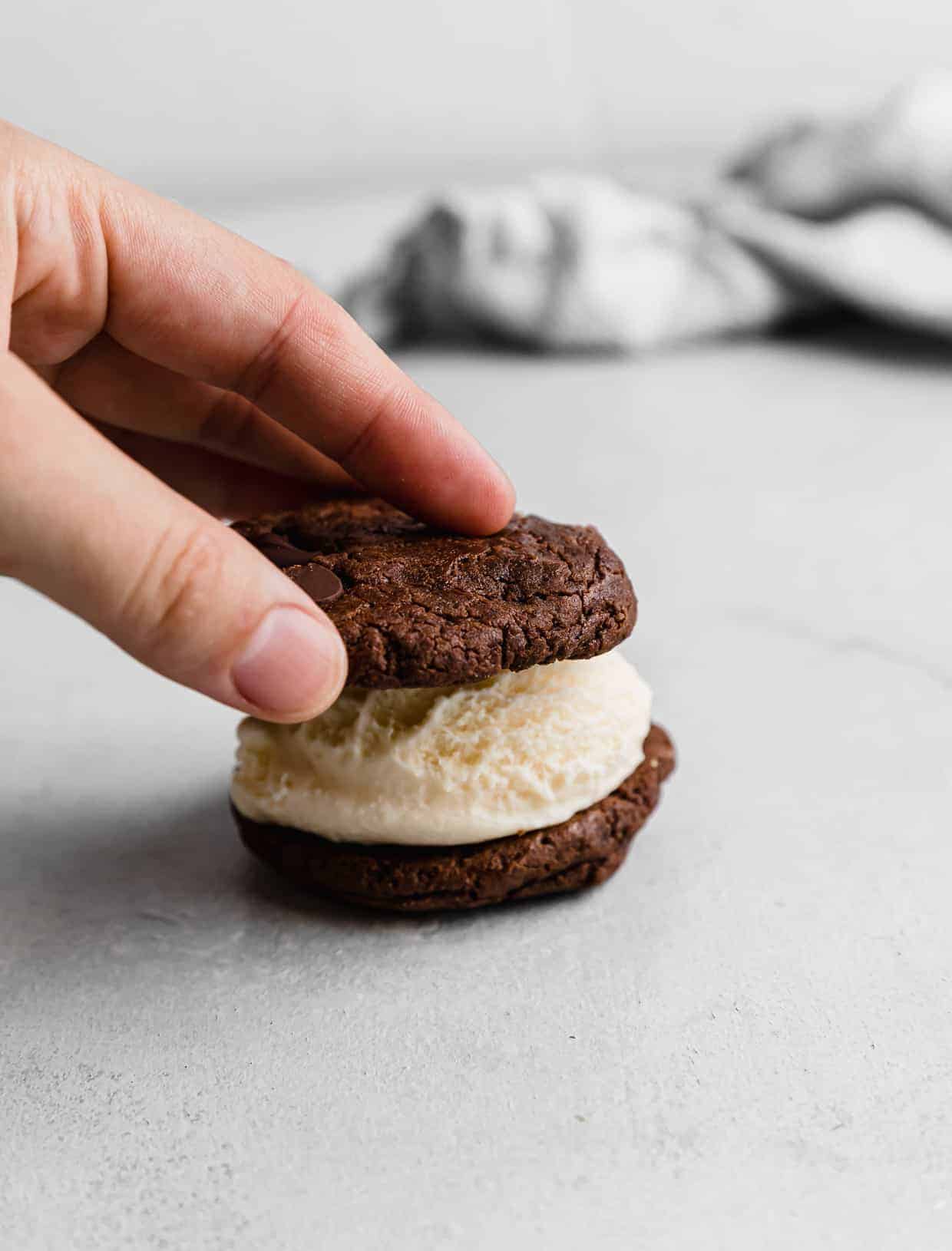 A hand pressing a chocolate cookie on top of a scoop of ice cream.