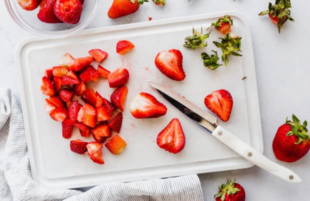 A cutting board with chopped strawberries and a white knife