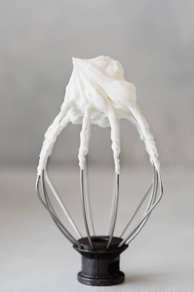 A Kitchen Aid whisk standing on its base with freshly whipped cream on the tip.