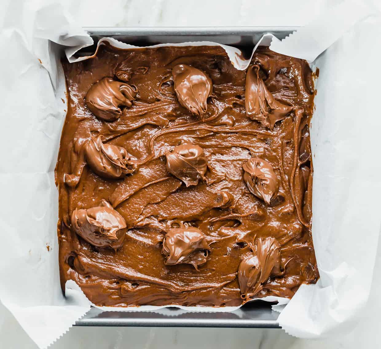 Nutella Brownie batter in an 8x8 pan, with dollops of Nutella along the top.