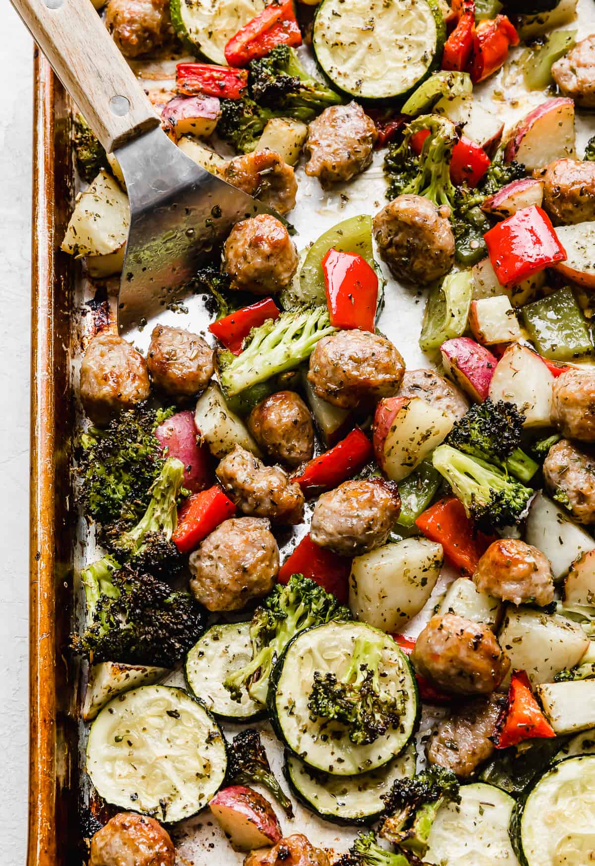 Sheet Pan Sausage and Veggies with a metal spatula scooping up some of the veggies.