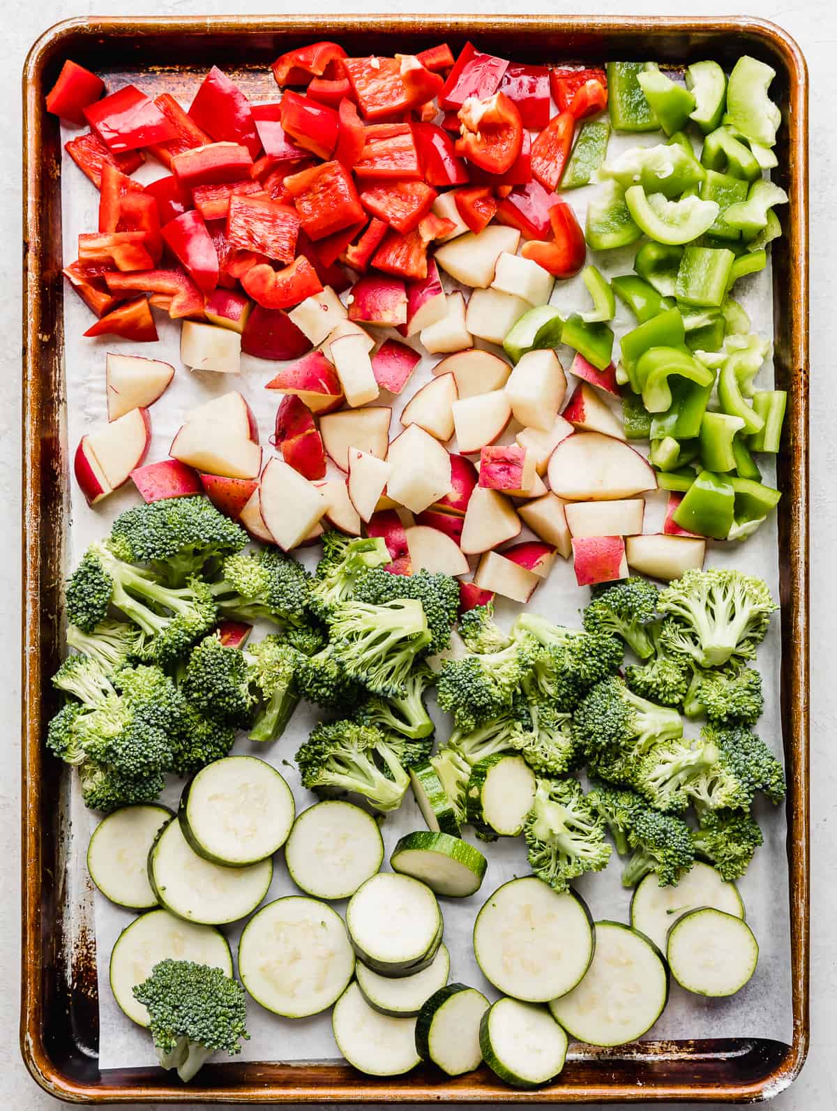 A baking sheet with red and green peppers, cut potatoes, broccoli florets and coin zucchini slices.