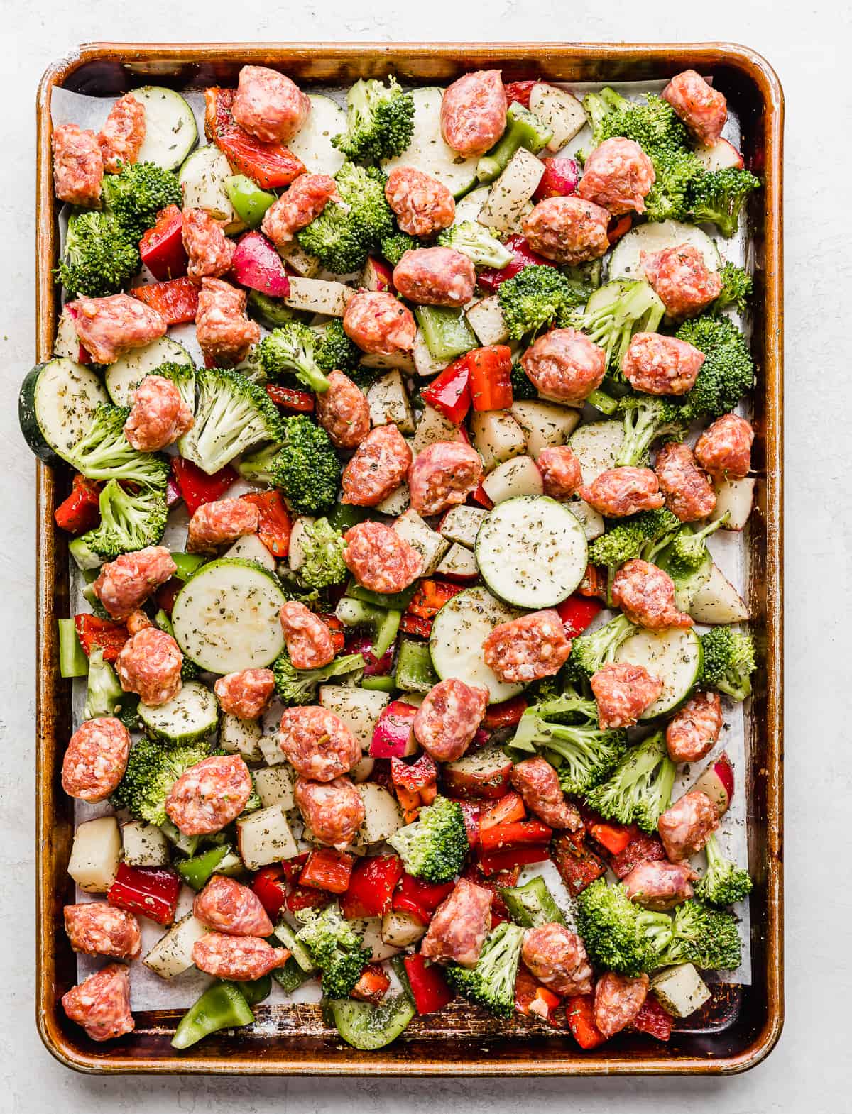 Unbaked Italian sausage and chopped veggies on a baking sheet.