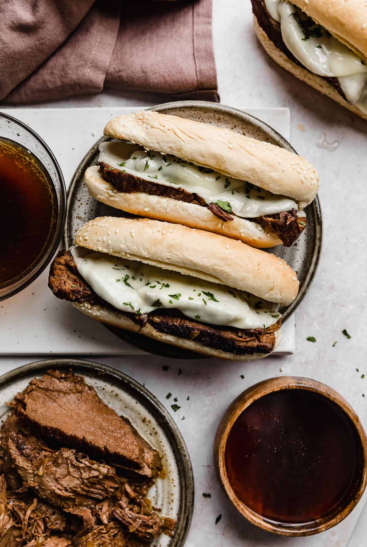 Two Slow Cooker French Dip Sandwiches on a gray plate with two bowls of au juice beside it.