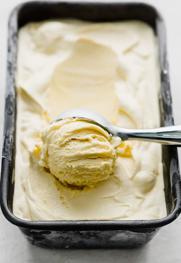 An ice cream scoop scooping out a portion of homemade vanilla ice cream.