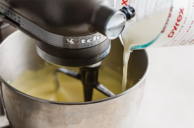 Warm cream being poured into a large bowl full of sugar and egg yolks, for making vanilla ice cream.