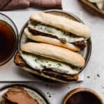Two Slow Cooker French Dip Sandwiches topped with melty provolone cheese on a gray plate.
