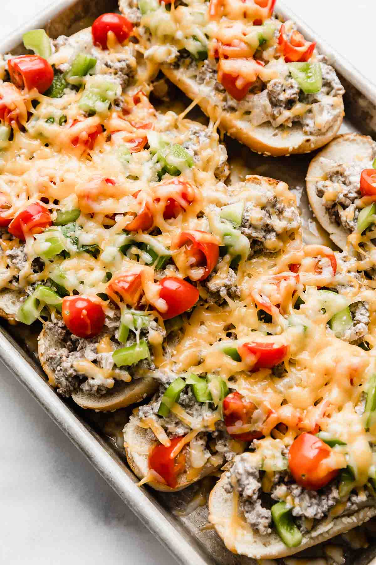 Beef Stroganoff Sandwiches on a baking sheet, each hoagie bun topped with ground beef mixture, diced tomatoes and green peppers, and melted cheddar cheese.