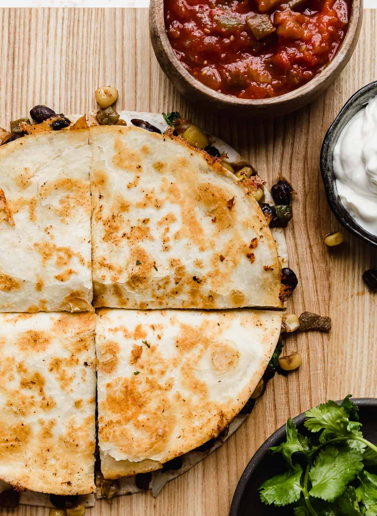 Close up photo of a Black Bean and Corn Quesadillas cut into wedges on a brown cutting board.