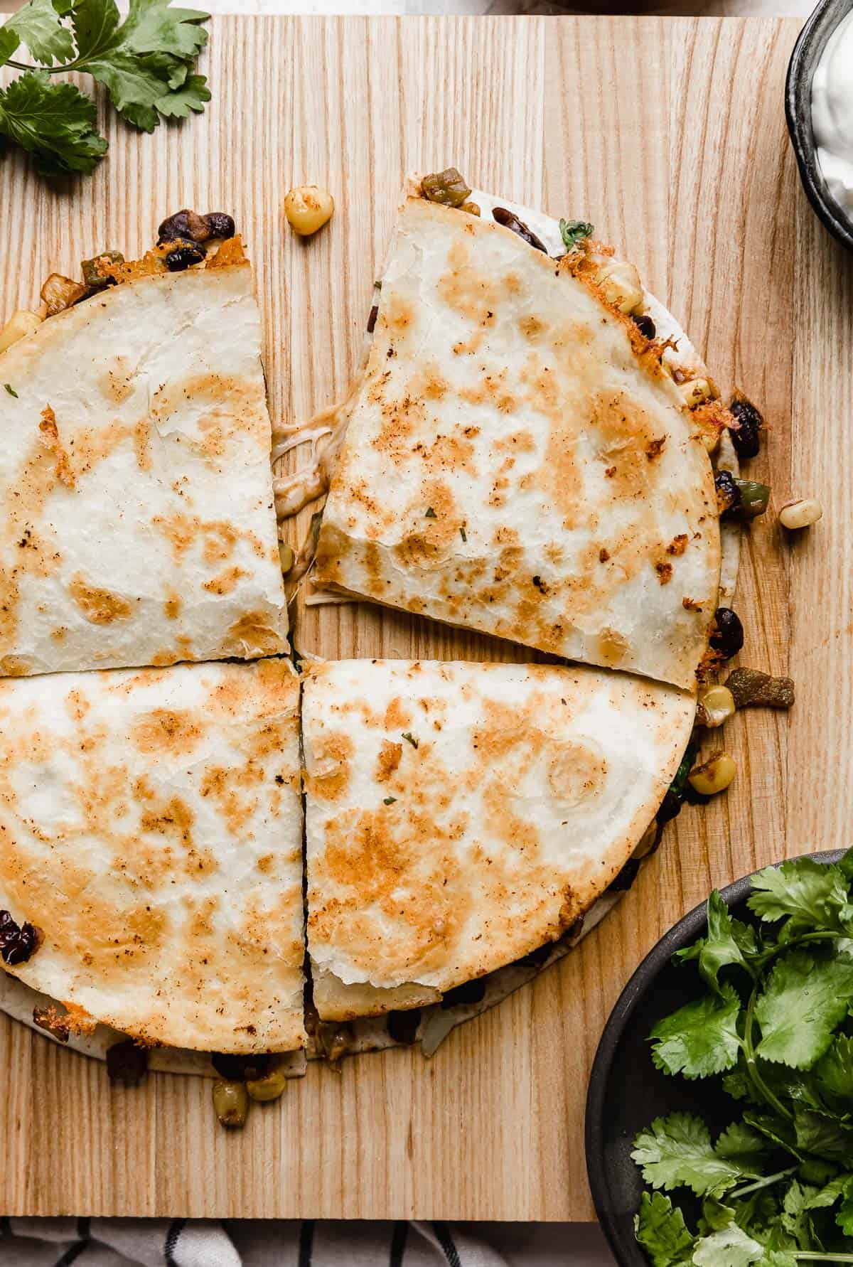 A Black Bean and Corn Quesadilla on a brown boat surrounded by cilantro.