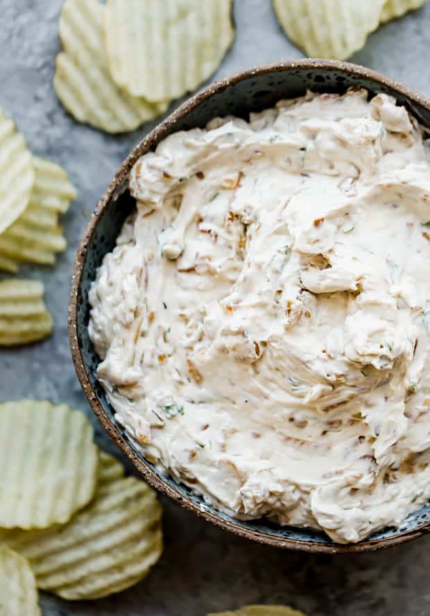 Onion dip in a bowl with ruffled potato chips around the bowl.