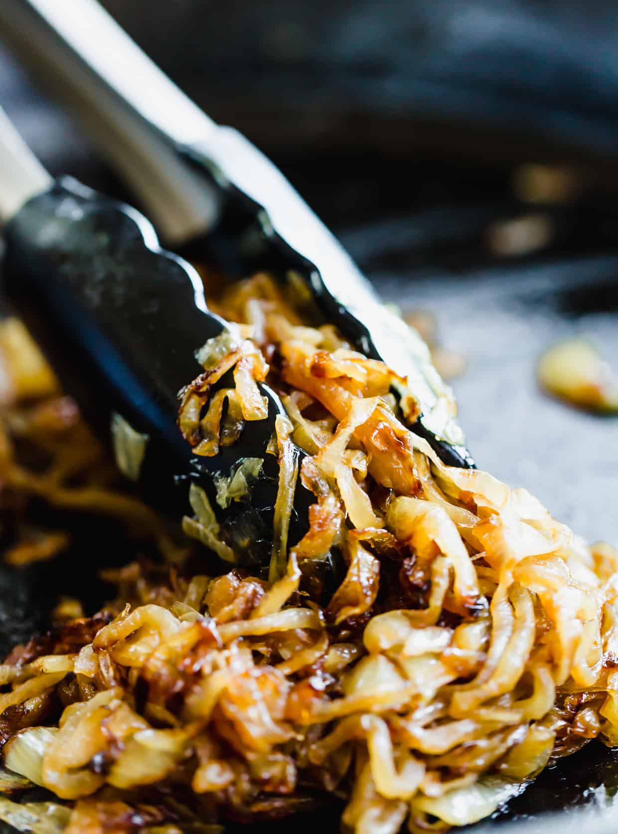 Fully caramelized onions with tongs grasping some of the onions.