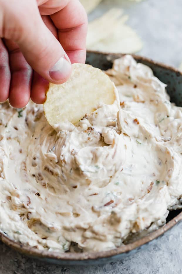 Onion dip in a bowl with a ruffled potato chip dipping into it.