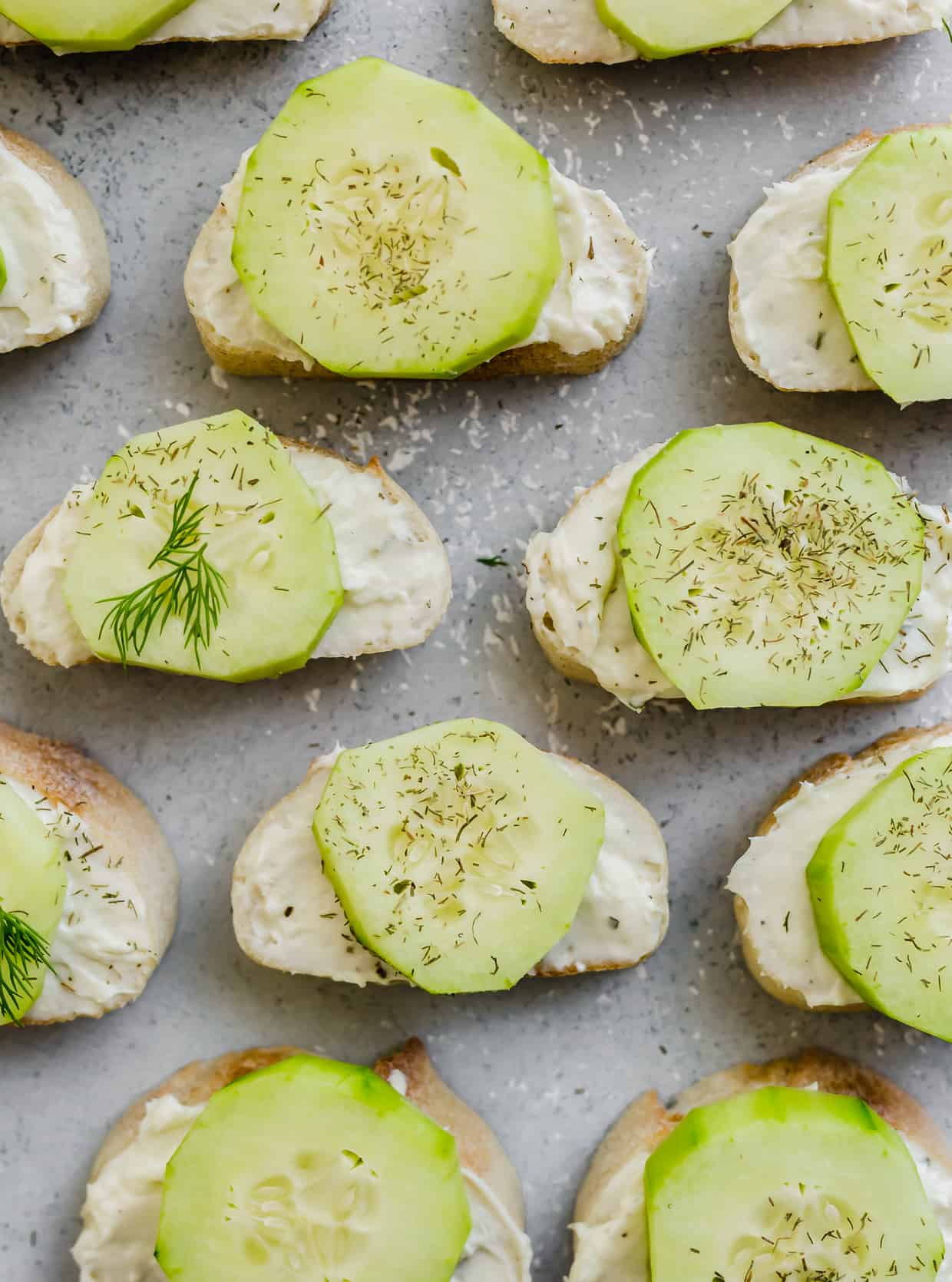 A collection of sliced cucumbers atop a cream cheese mixture on a sliced baguette. 