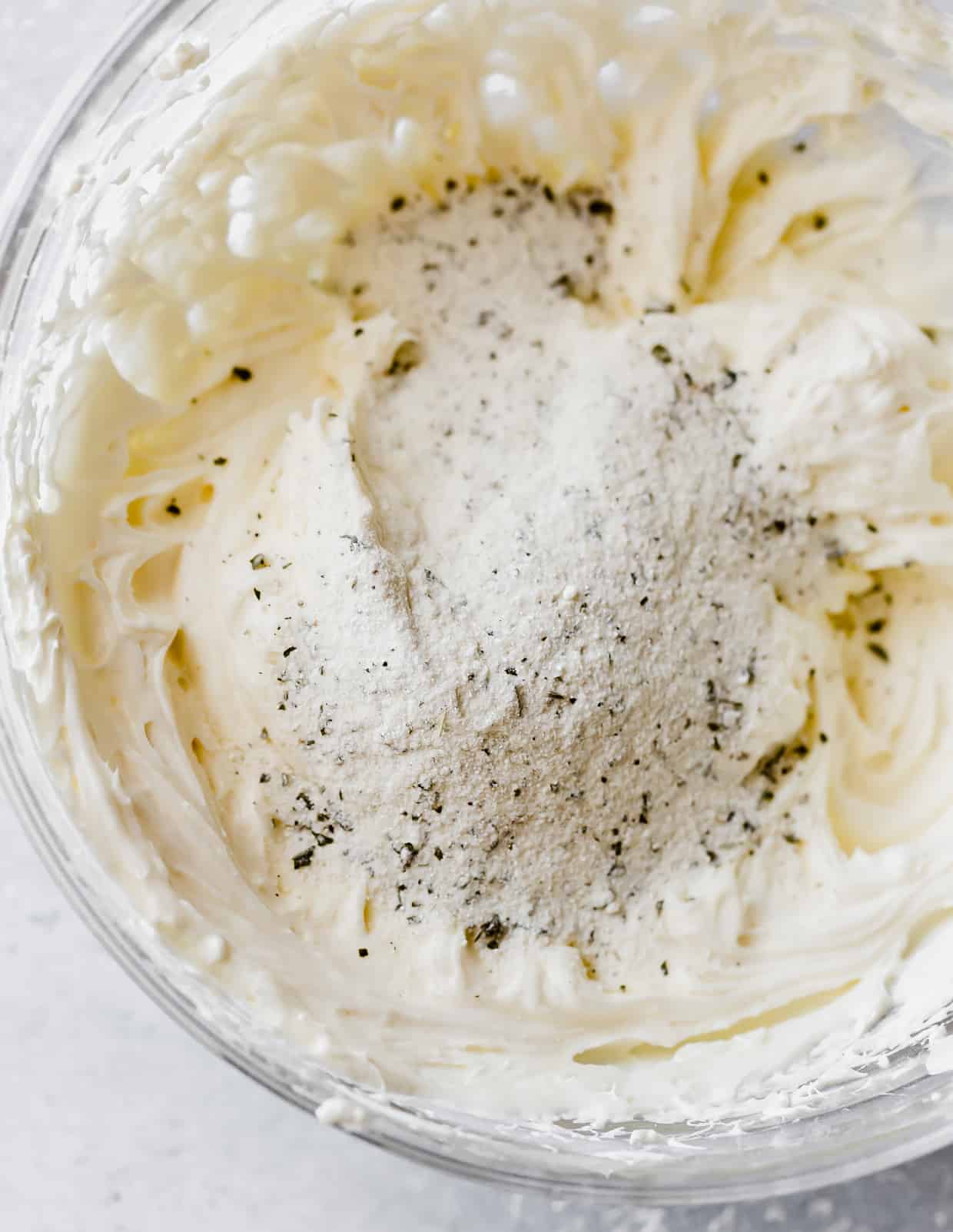 Dried ranch seasoning mix atop a cream cheese and mayonnaise mixture in a bowl.
