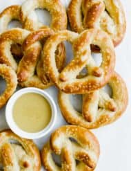 Homemade pretzels baked to golden brown, stacked in a heap with a bowl of honey mustard in the midst of the pretzels.