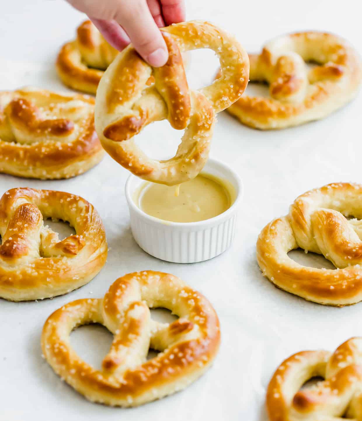 A golden brown pretzel sprinkled with coarse salt being dipped into a small bowl of honey mustard sauce.