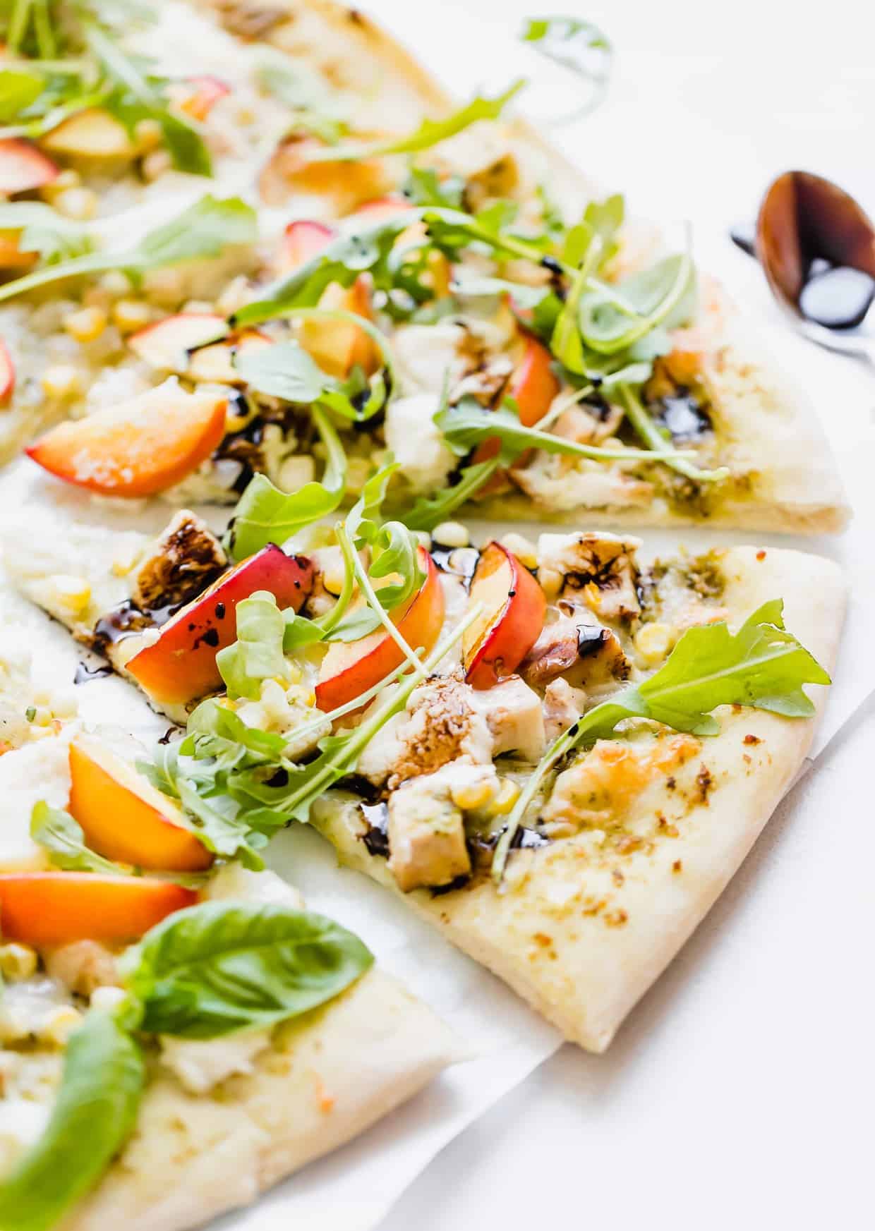 Slice of pizza topped with diced chicken, corn, nectarines, ricotta, and arugula.