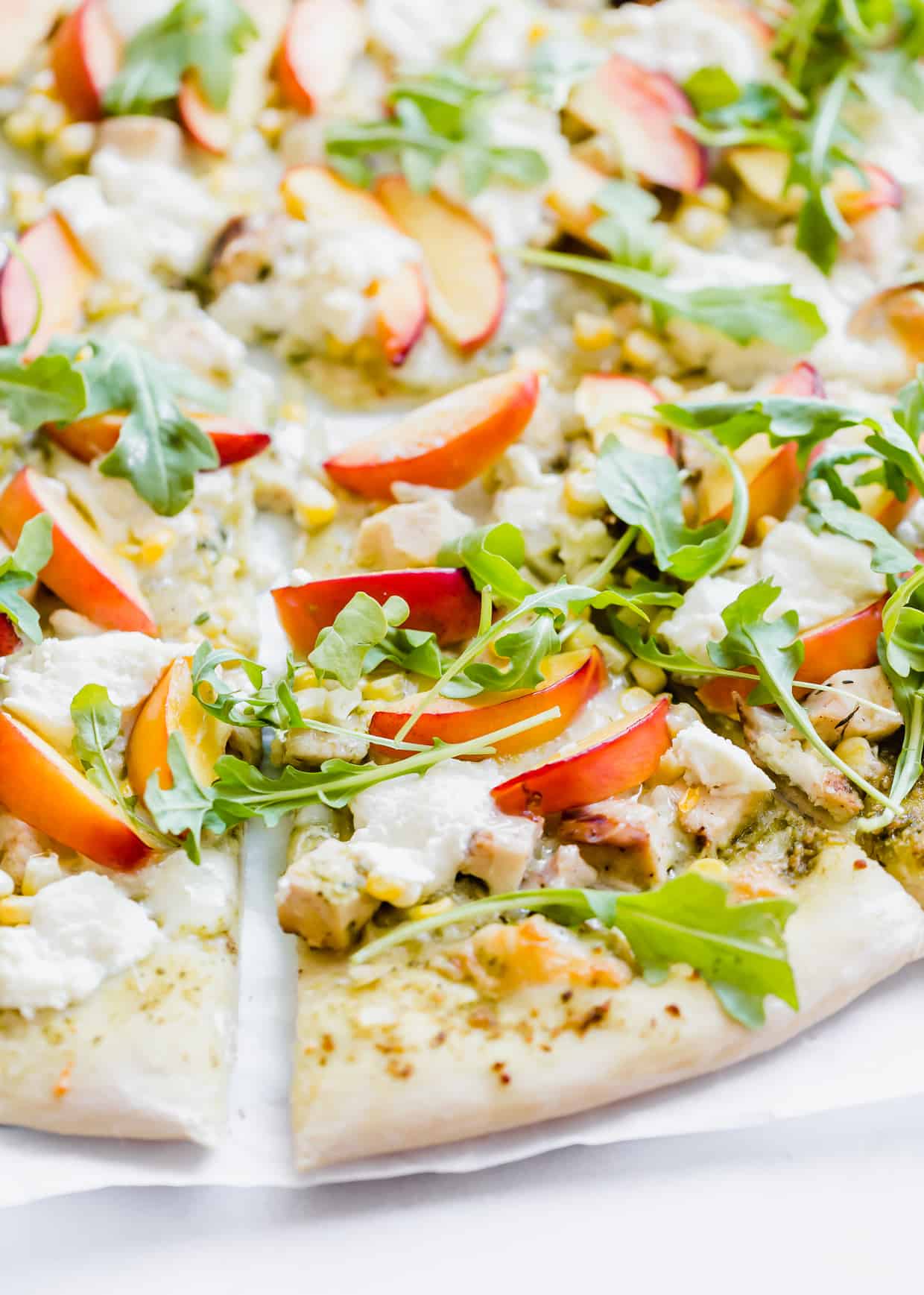 Slice of pizza topped with ricotta, arugula, and nectarines. 